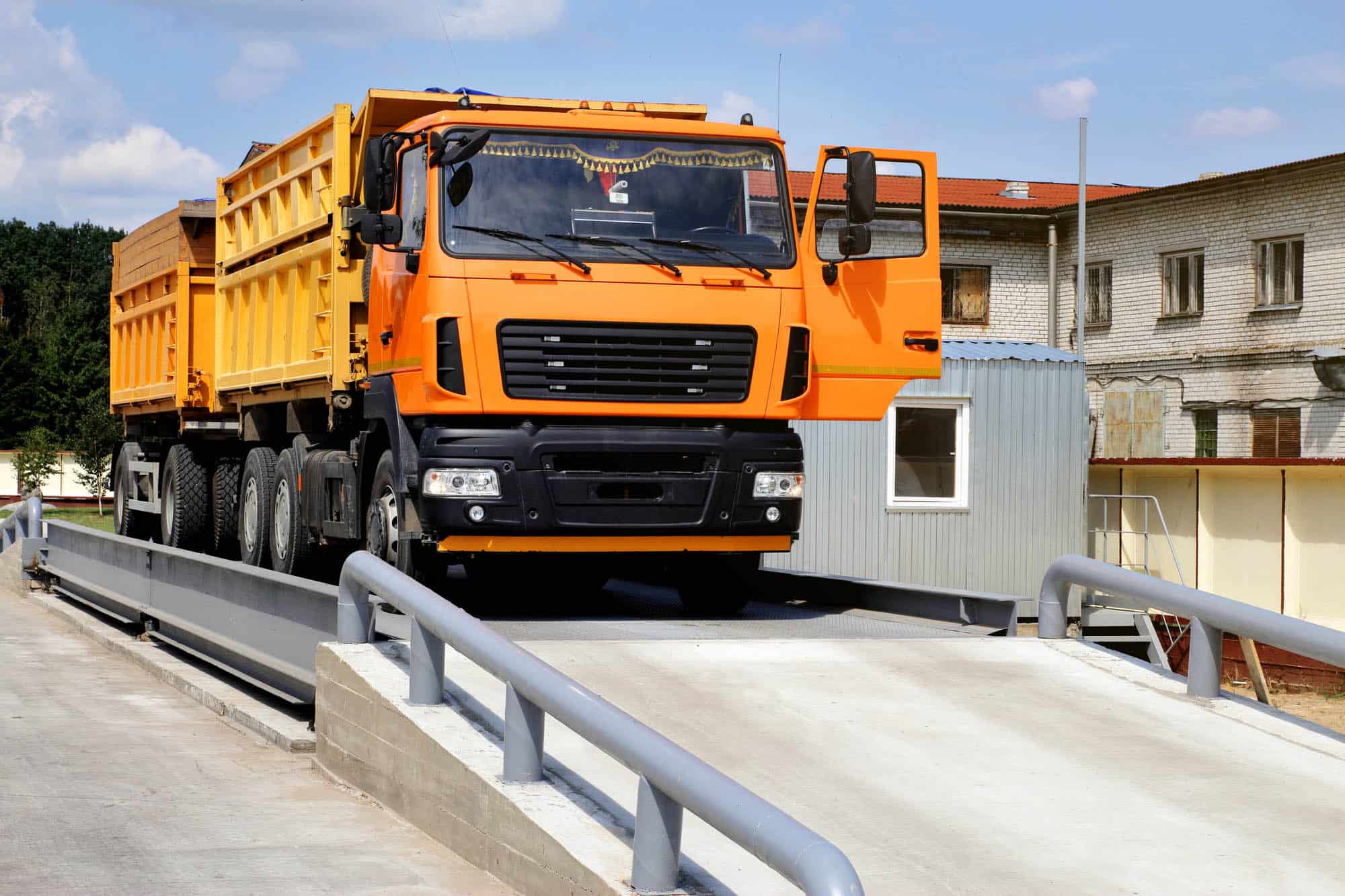 orange truck with grain is weighed on the scales in the grain storage area. Truck scales